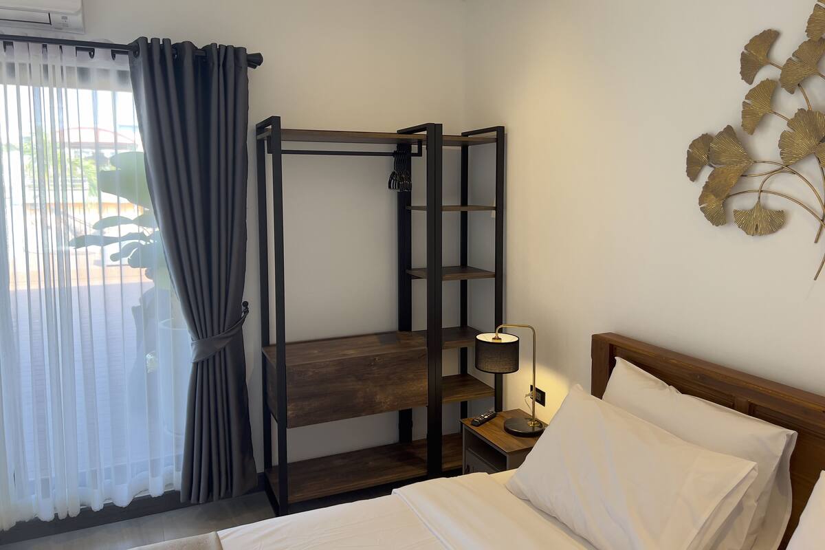A hotel room with a bunk bed, a bedside table with a lamp, and a wall-mounted shelf.