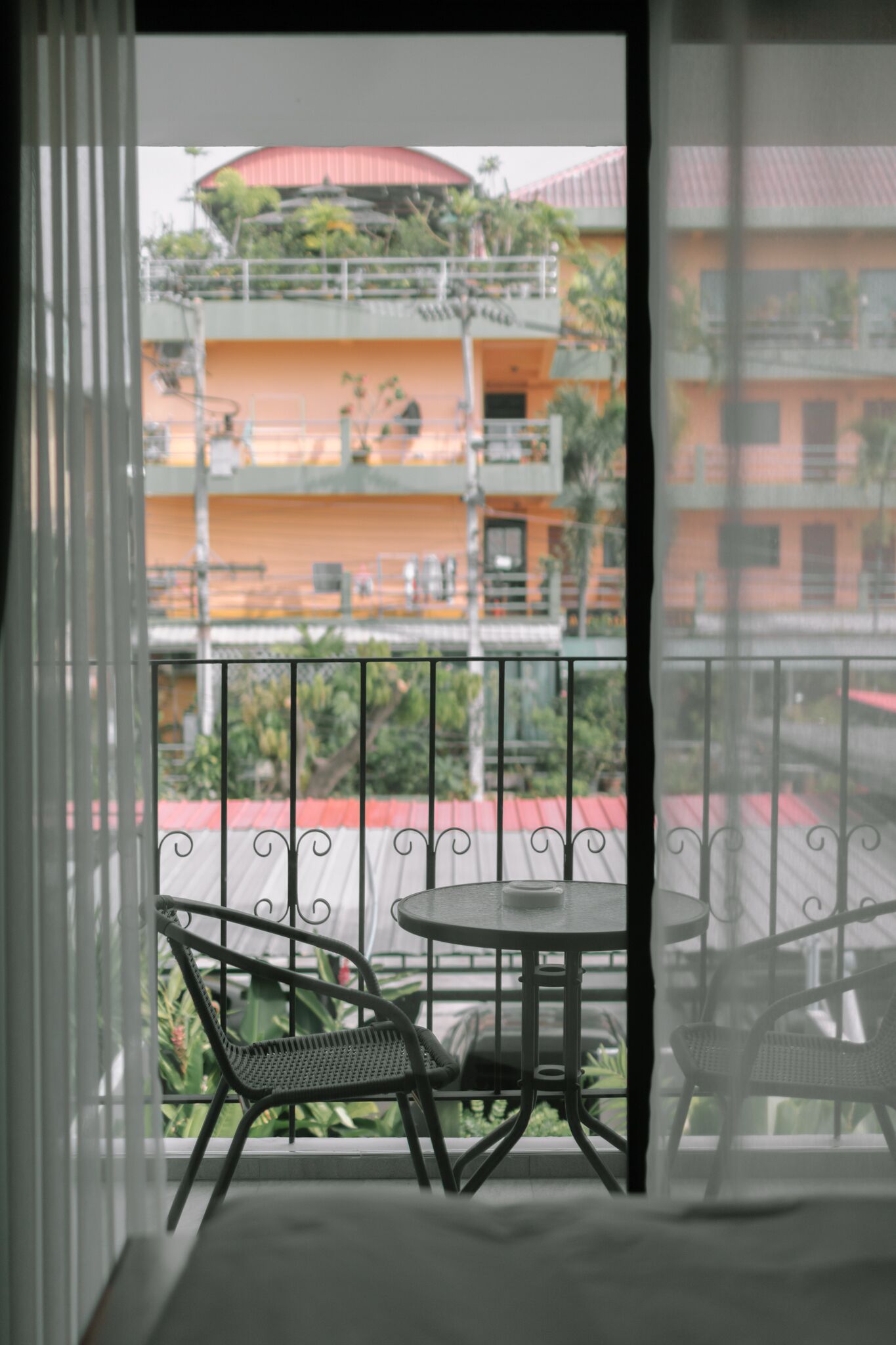A balcony with a round table and two chairs, overlooking a building with multiple balconies and a red roof.