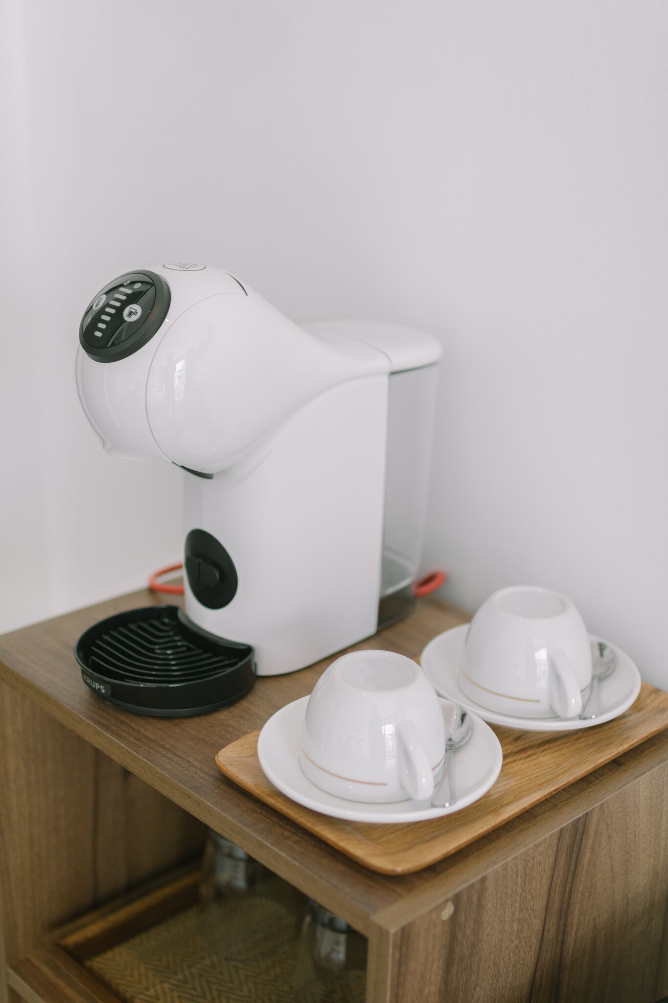 A white coffee maker on a wooden table with two white cups and saucers.
