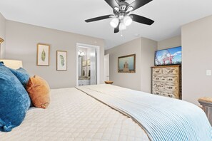 Ein Schlafzimmer mit Bett, Deckenventilator, gerahmten Bildern, Kommode und Fernseher.