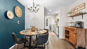 A dining area with a round table, two chairs, a chandelier, and a coffee bar with a sign. - 3BR Ozark View Condo | Near Branson Strip (Branson)