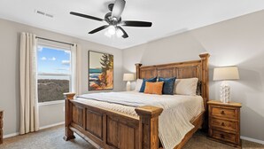 A bedroom with a wooden bed, a ceiling fan, a nightstand with a lamp, and a window with curtains. - 3BR Ozark View Condo | Near Branson Strip (Branson)
