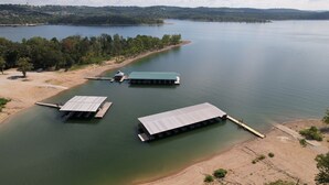 A lakeside property with three docked boats, a sandy beach, and a forested area in the background.