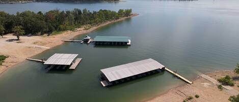 A lakeside property with three docked boats, a sandy beach, and a forested area in the background.
