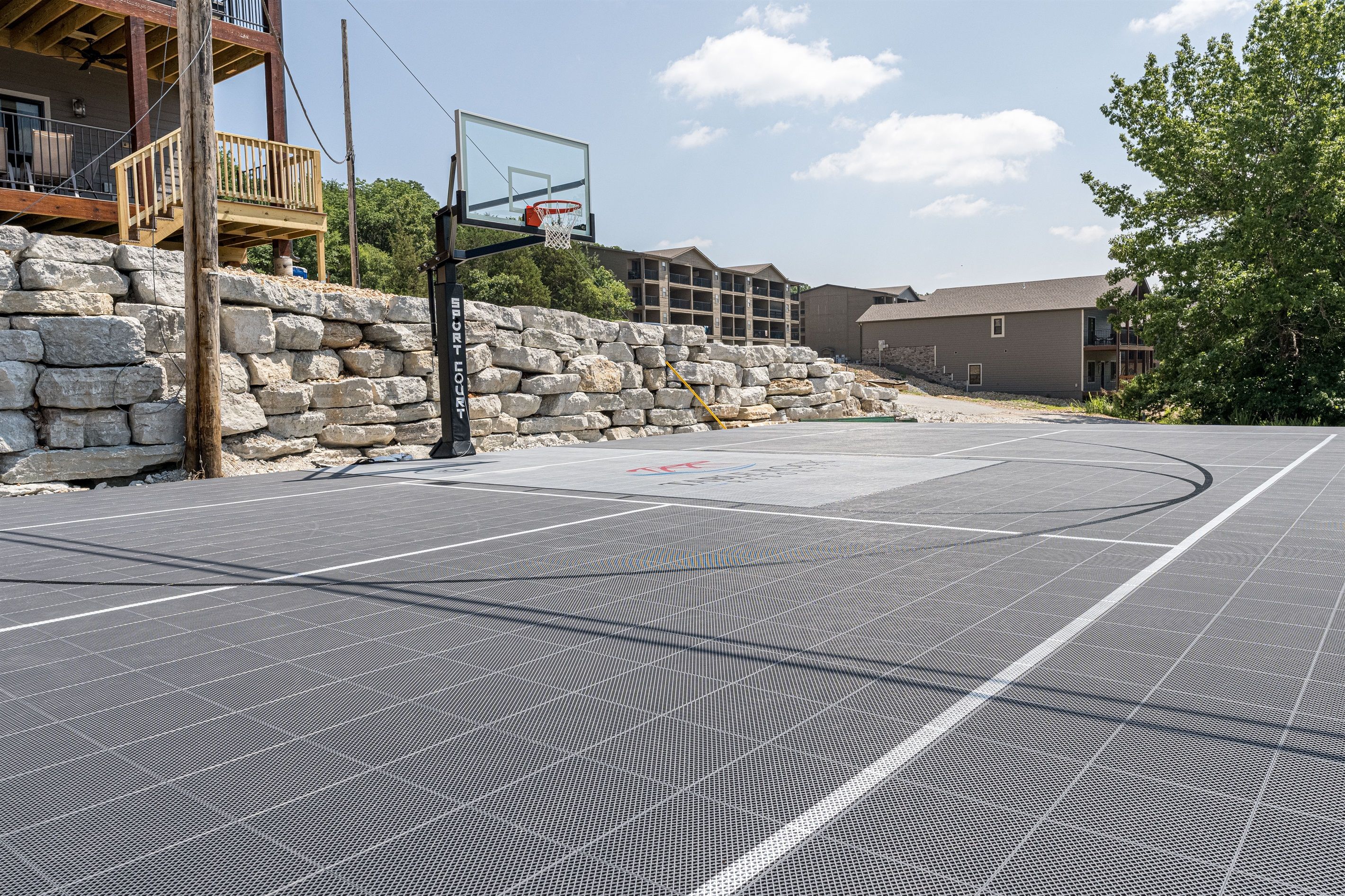 An outdoor basketball court with a stone wall and a wooden deck.