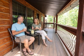 A wooden deck with a railing, a table with drinks, and a view of greenery.
