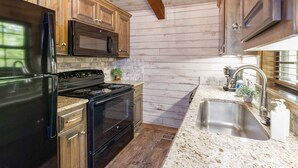 A kitchen with wooden cabinets, a black refrigerator, a microwave, a stove, and a sink.