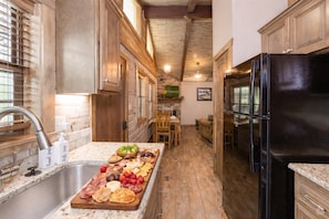 A narrow kitchen with wooden cabinets, a black refrigerator, and a long countertop with a charcuterie board.