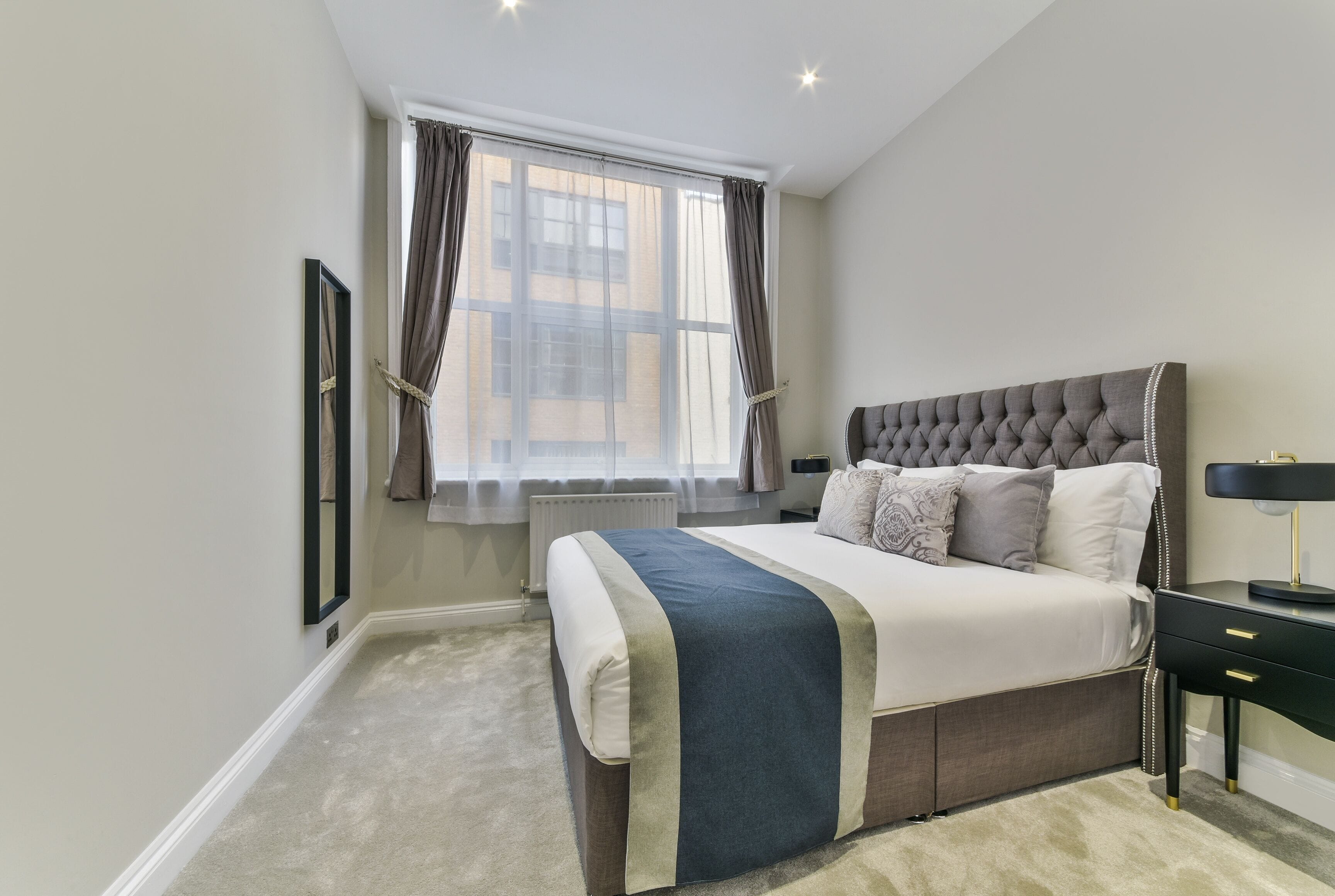 A bedroom with a large bed, a nightstand, a lamp, and a window with curtains.