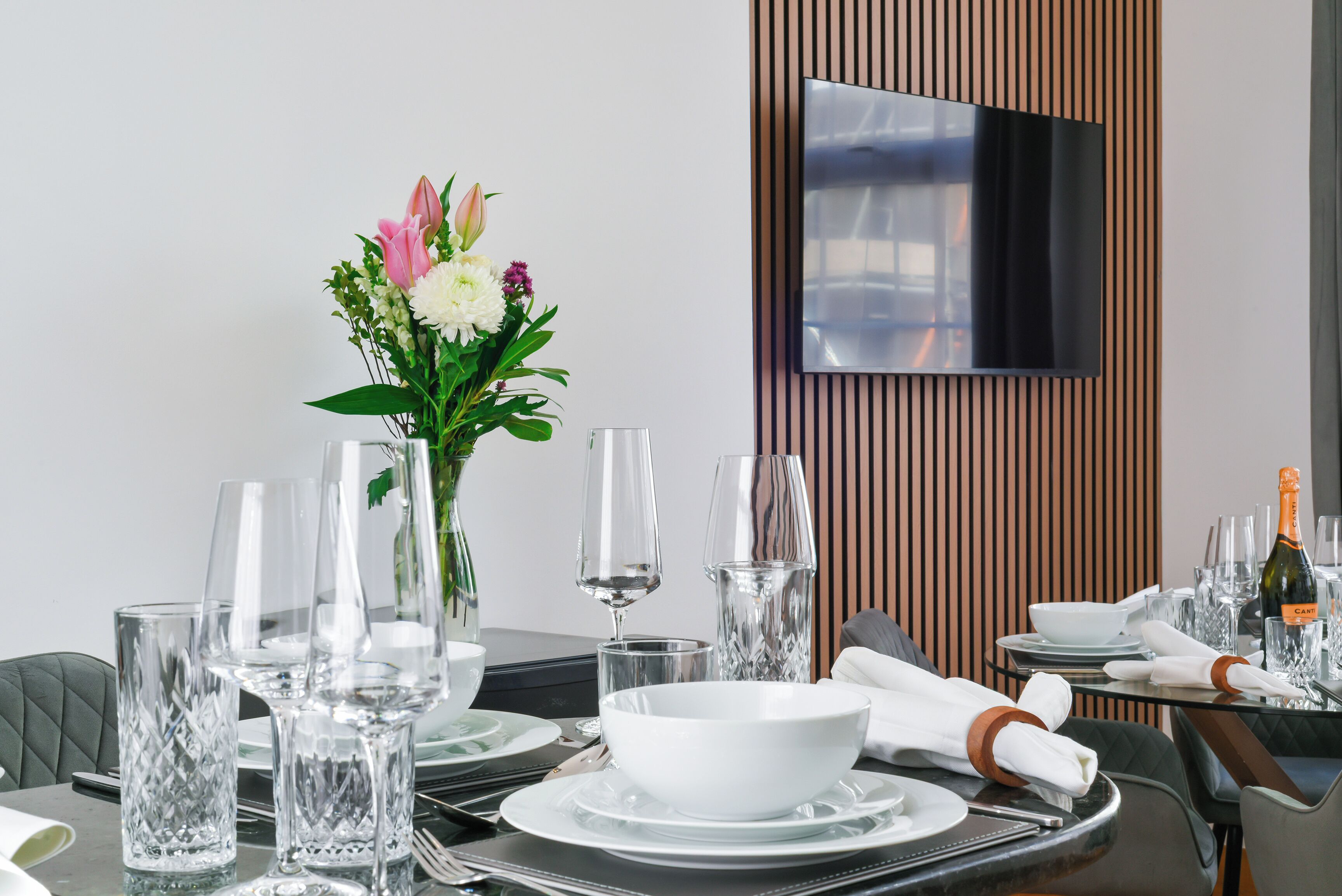 Een eettafel gedekt met helder glaswerk, witte borden en een bloemstuk als decoratie.
