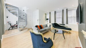 Uma sala de estar moderna com escada, um sofá cinza, uma poltrona azul e uma mesa de jantar.