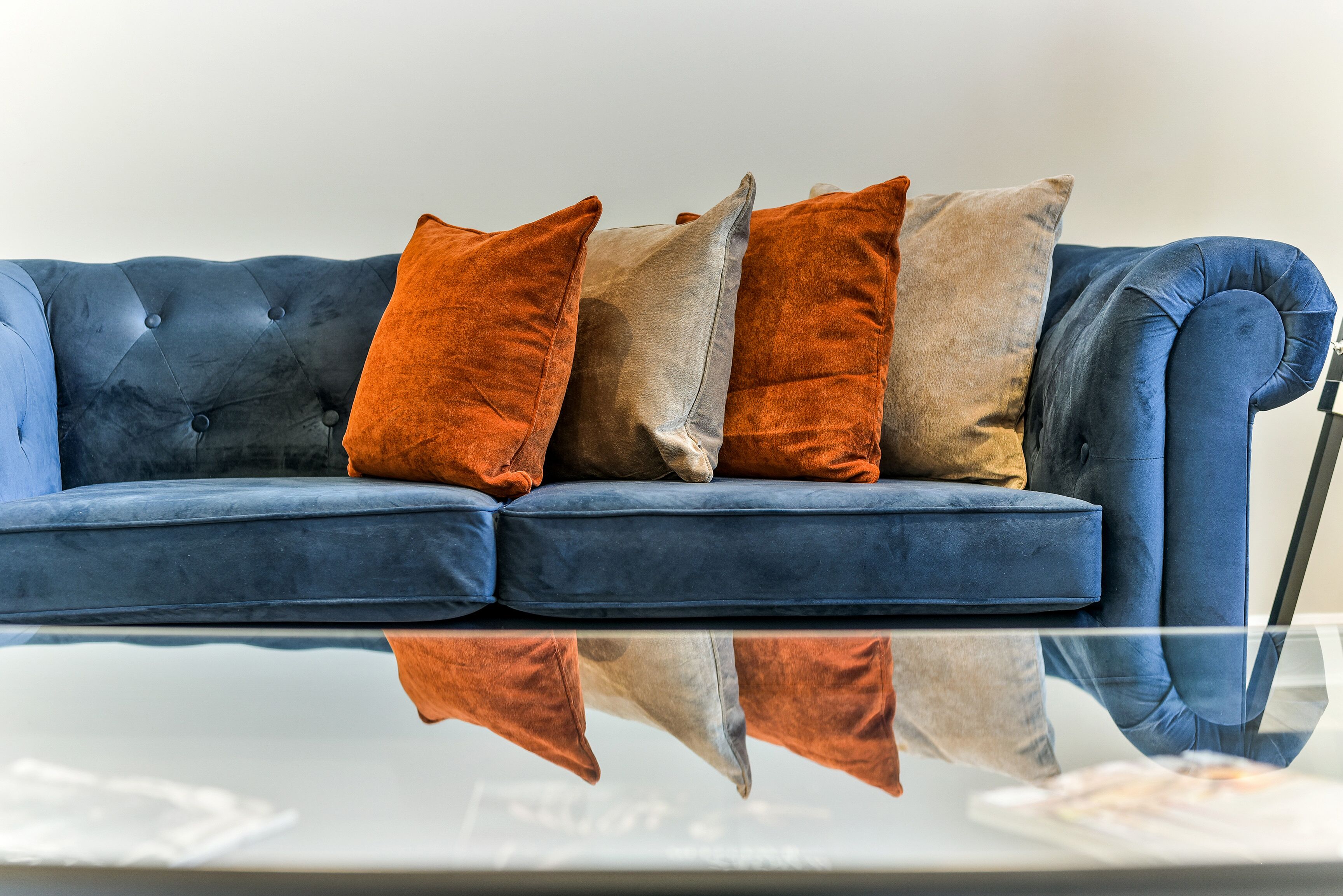 A blue sofa with four cushions in shades of orange and beige.