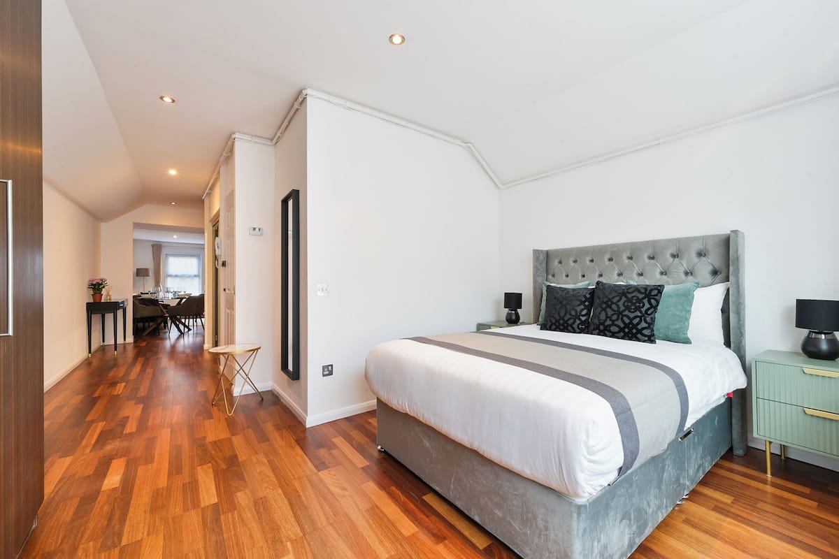 A modern bedroom with a large bed, a green nightstand, and a dining area in the background.