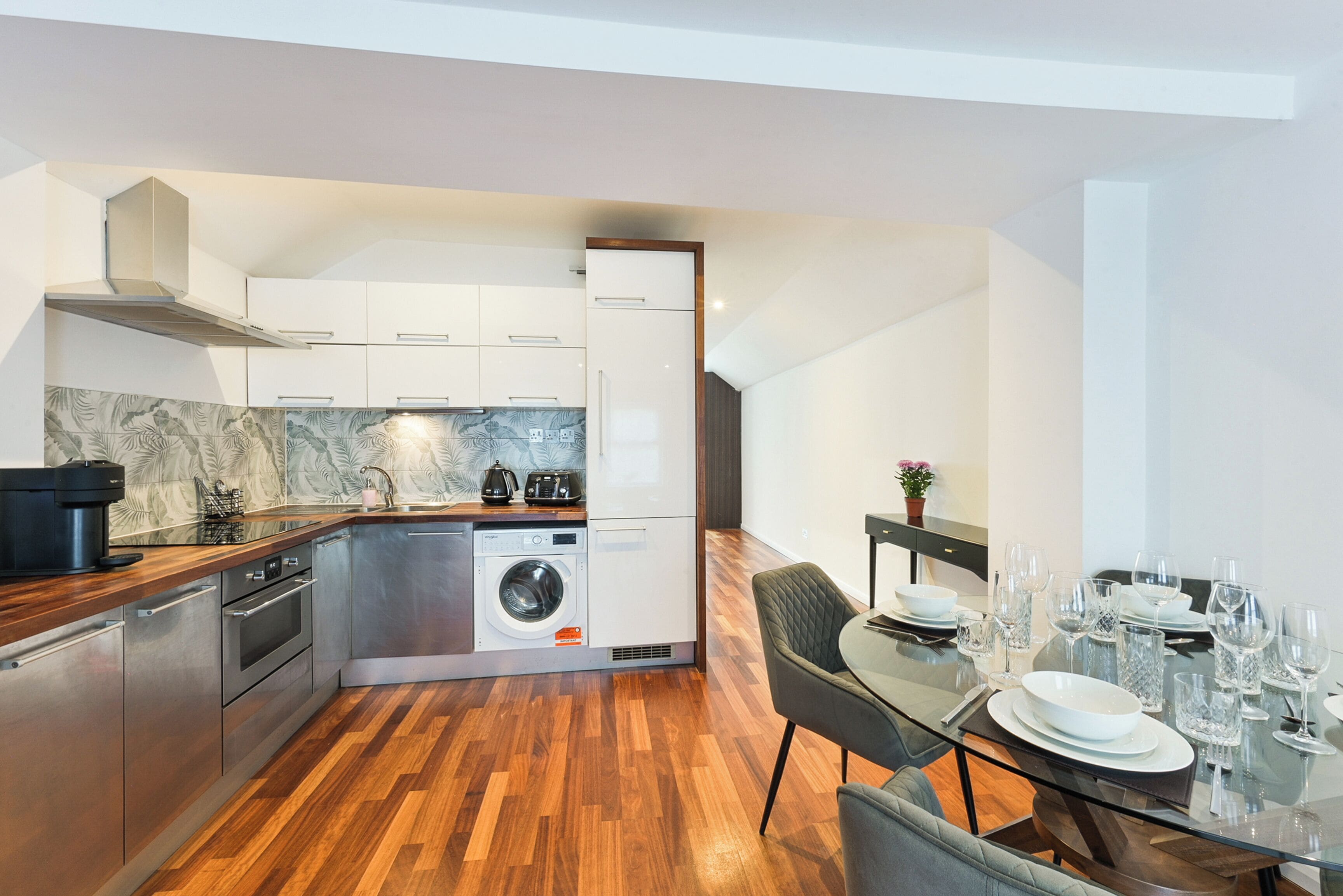 Una cocina moderna con electrodomésticos de acero inoxidable, lavadora integrada y comedor con mesa de vidrio para seis personas.
