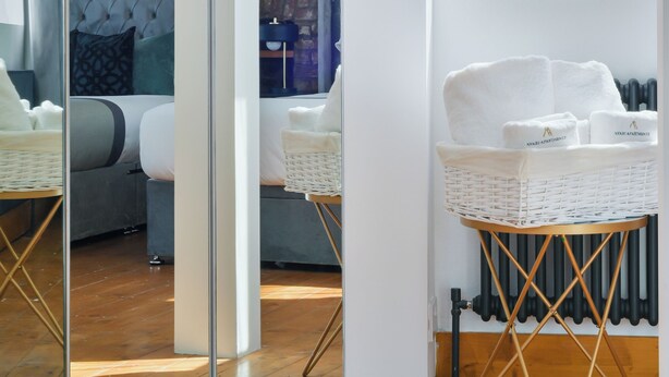 Quarto de hotel moderno com guarda-roupa espelhado, parede de tijolos, cama com cabeceira estofada, mesa de cabeceira de vime branco e radiador.