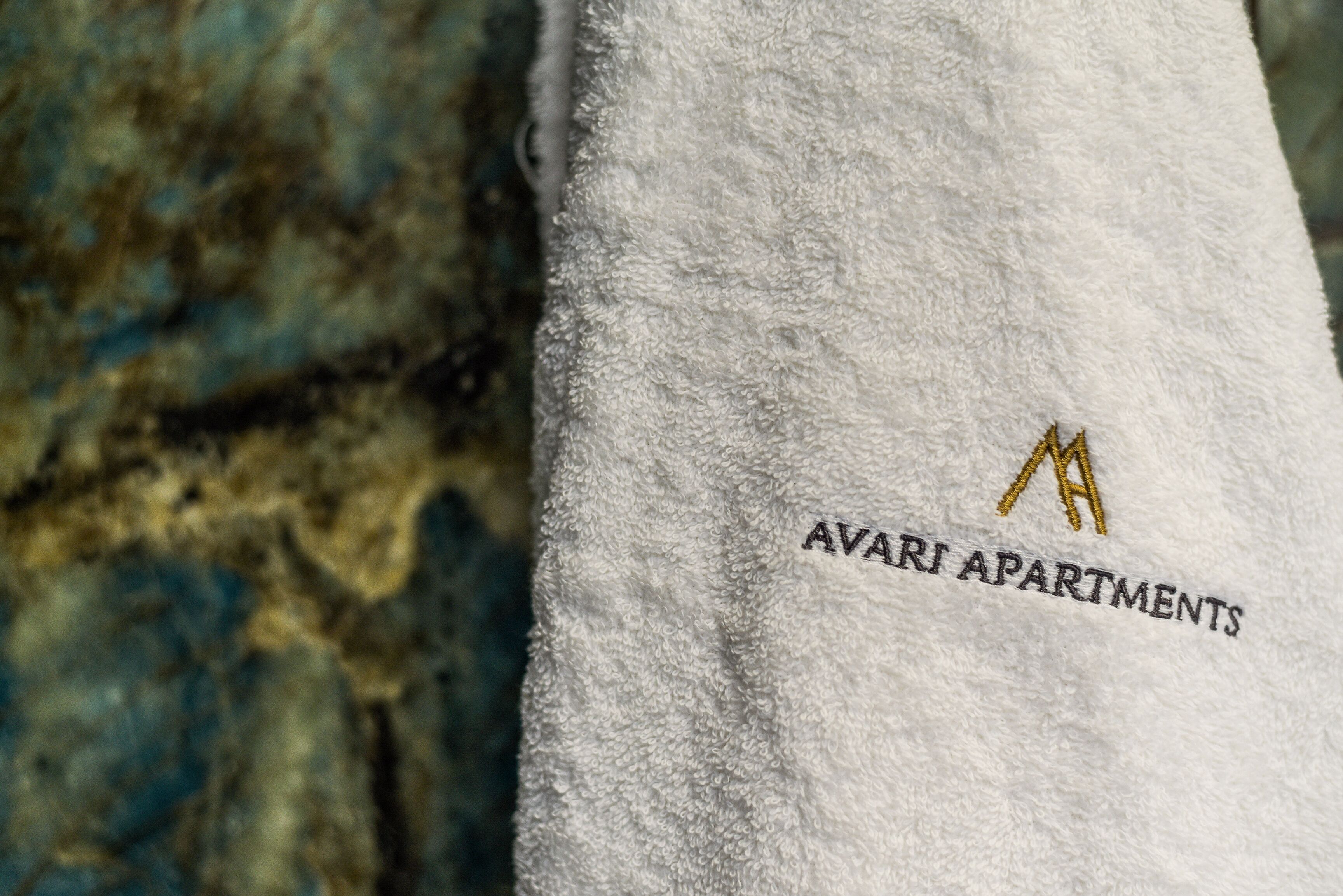 A white towel with embroidered text "AVARI APARTMENTS" and a gold logo.
