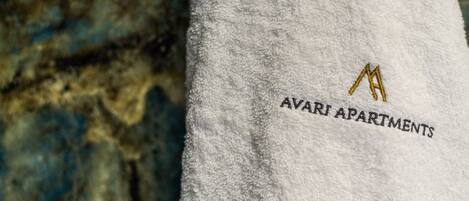 A white towel with embroidered text "AVARI APARTMENTS" and a gold logo.