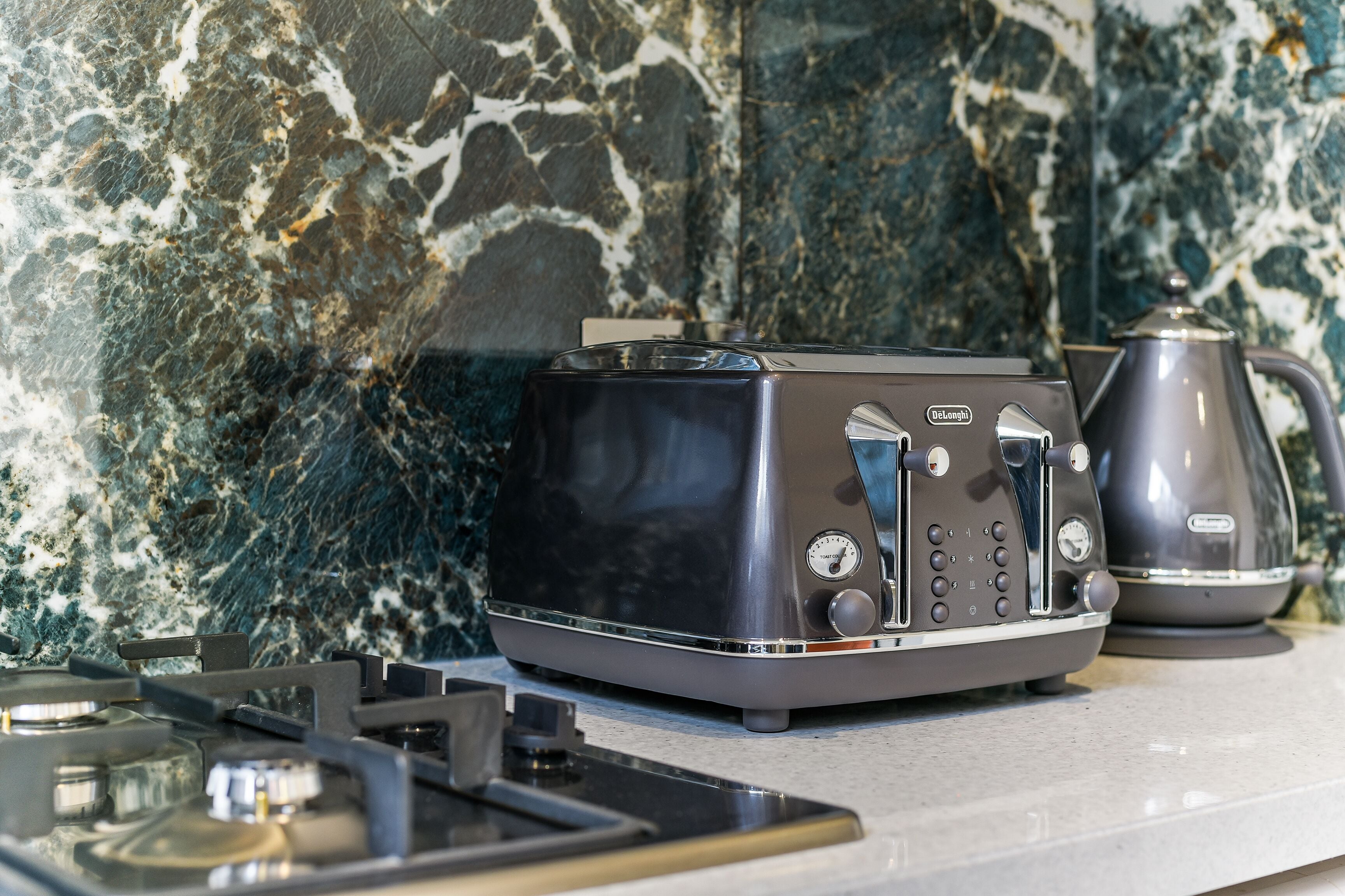 Une cuisine équipée d’une machine à expresso moderne, d’une bouilloire et d’un dosseret en marbre.