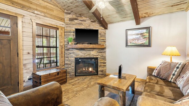 Una sala de estar acogedora con chimenea de piedra, muebles de madera y un ventilador de techo.