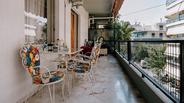 Een balkon met een tafel en stoelen, uitzicht op de straat, en een gebouw op de achtergrond.