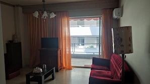 Een woonkamer met een televisie, een bank, een salontafel en een balkon met gordijnen.