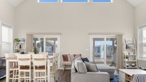 A spacious living area with a high ceiling, a dining table with chairs, a sofa, and a bookshelf. - Nautical Lane 146 by Seaside Vacations & Sales (Ocean City)