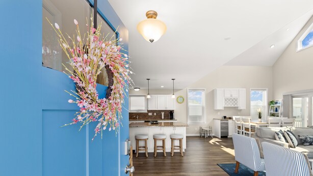 A modern kitchen with white cabinets, a central island with stools, and a dining area with a sofa and striped chairs. - Nautical Lane 146 by Seaside Vacations & Sales (Ocean City)