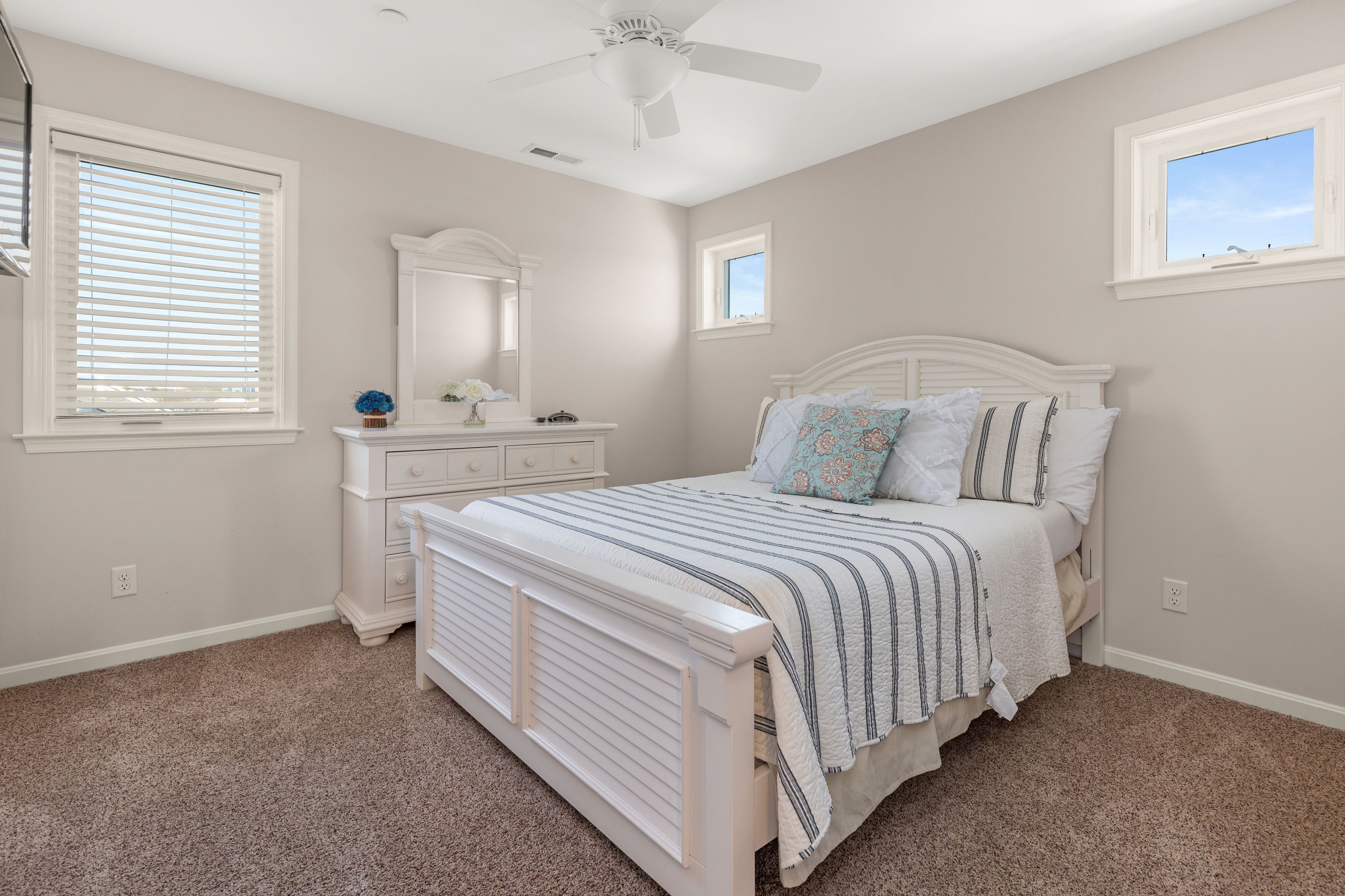 A bedroom with a white bed, a dresser, a mirror, and a ceiling fan.