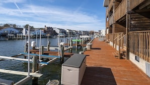 A wooden dock extending into calm water with boats docked, a small building with a wooden facade, and a clear sky. - Newport Bay 5 by Seaside Vacations & Sales (Ocean City)