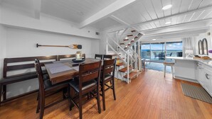 Un coin repas avec une table et des bancs en bois, une cuisine avec des meubles blancs et un escalier menant à un balcon offrant une vue panoramique.
