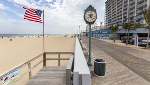 A boardwalk with a clock, an American flag, and a beach in the background.
