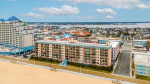 A beachfront hotel with multiple floors, a swimming pool, and a view of the ocean and cityscape.