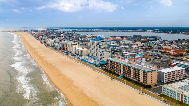A coastal cityscape with a beachfront hotel featuring multiple floors, a swimming pool, and a view of the ocean.