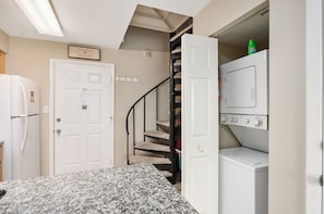 A laundry room with a washer and dryer, a white door with a sign, a staircase with a cat tree, and a refrigerator.