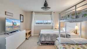 Quarto com beliche, televisão em uma cômoda, janela com cortinas e ventilador de teto.