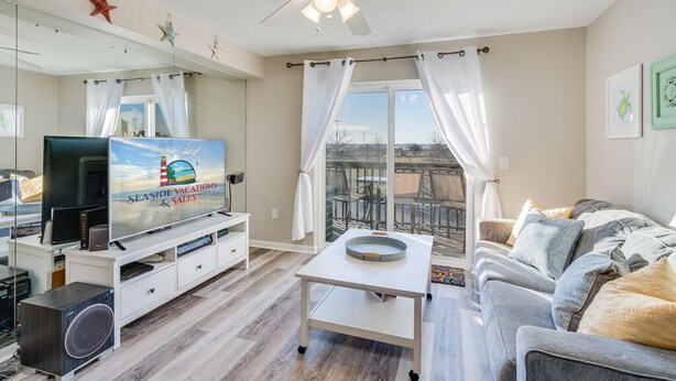 Uma sala de estar com televisão, ventilador de teto, mesa de jantar e sofá.