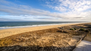 Une plage avec un sentier sablonneux menant au rivage, une clôture le long de la plage et l’océan en arrière-plan.