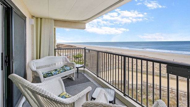 Un balcon agrémenté de meubles en osier, une vue sur la plage et un ciel dégagé.