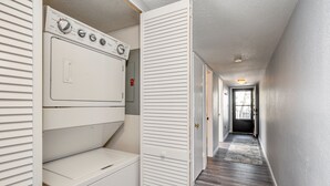 A laundry room with stacked washers and dryers, a door leading to a hallway, and a view of a building outside.