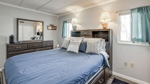 A bedroom with a bed, dresser, bedside lamps, and a window with curtains.