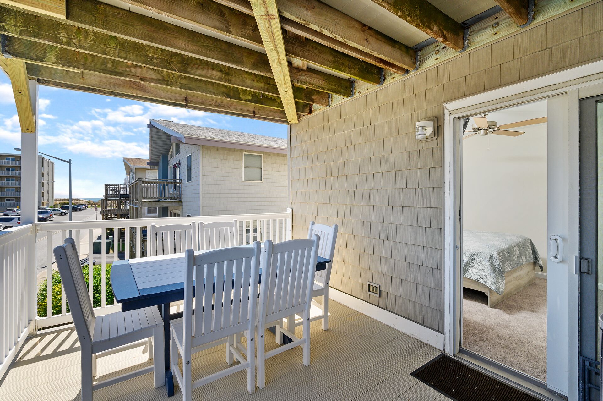 A covered outdoor area with a table and chairs, a door leading to a bedroom, and a view of other buildings.