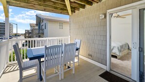 A covered outdoor area with a table and chairs, a door leading to a bedroom, and a view of other buildings. - Siesta Villa 101N by Seaside Vacations & Sales (Ocean City)