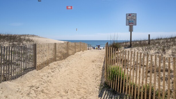 A sandy beach path with wooden fences on both sides, leading to the ocean. - Siesta Villa 101N by Seaside Vacations & Sales (Ocean City)