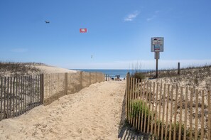 Un sentier de sable bordé de clôtures en bois de part et d’autre, qui mène à l’océan.