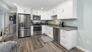 A modern kitchen with white cabinetry, stainless steel appliances, and a granite countertop. - Siesta Villa 101N by Seaside Vacations & Sales (Ocean City)