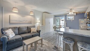 Un salon moderne avec un canapé gris, une petite table basse et un coin repas équipé de tabourets de bar.
