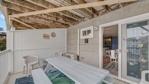 Un patio couvert avec une table et des bancs blancs, une petite chaise blanche, et une vue sur l’intérieur de la maison.