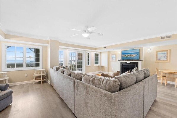 A spacious living room with a large sectional sofa, a ceiling fan, and a flat-screen TV. - Somerset on 2nd 202 by Seaside Vacations & Sales (Ocean City)