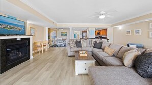 Un salon spacieux avec une cheminée, un grand canapé, un coin repas et une cuisine à l’arrière-plan.