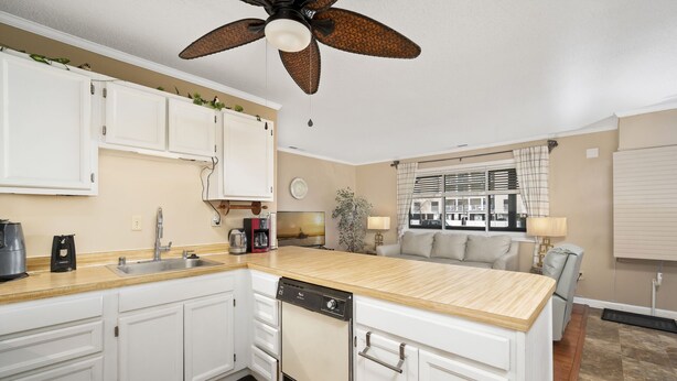 Une cuisine de taille réduite avec des meubles blancs, un plan de travail en bois, un lave-vaisselle et un ventilateur de plafond.